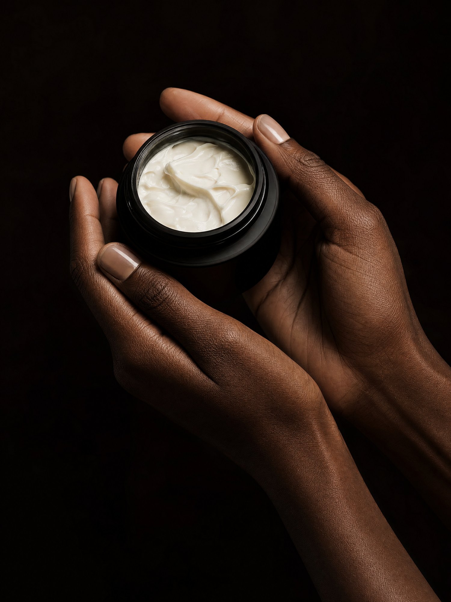 Hands holding an open jar of MelaSil cream, warm editorial light